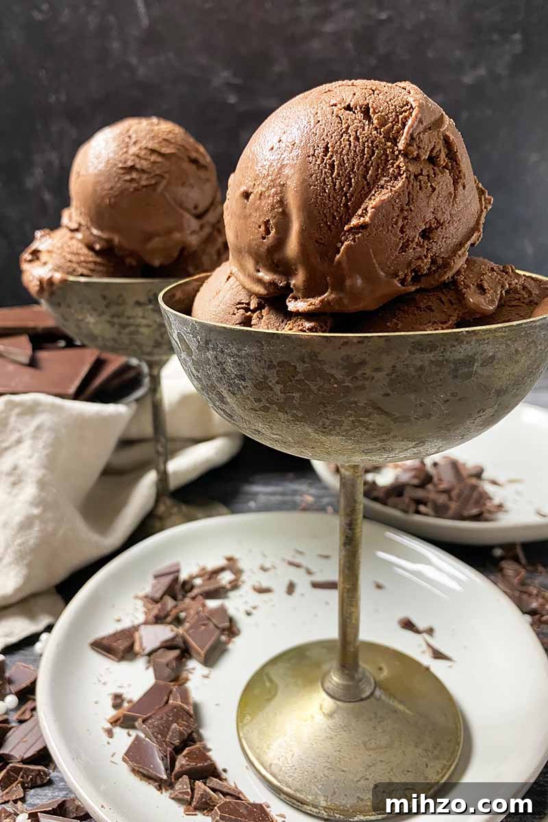 Vertical image of metal goblets with scoops of a dark brown frozen dessert on white plates.