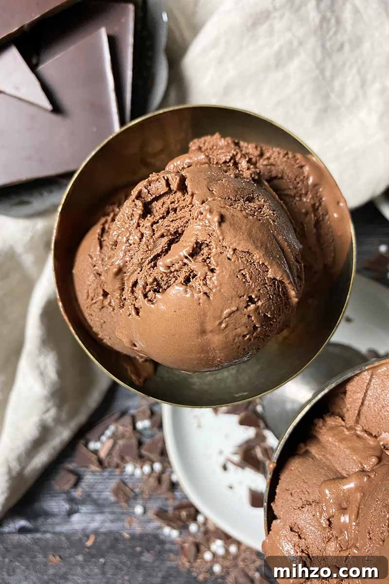 Vertical top-down image of a bowl with scoopfuls of a cocoa frozen dessert next to a chocolate bar and tan towel.