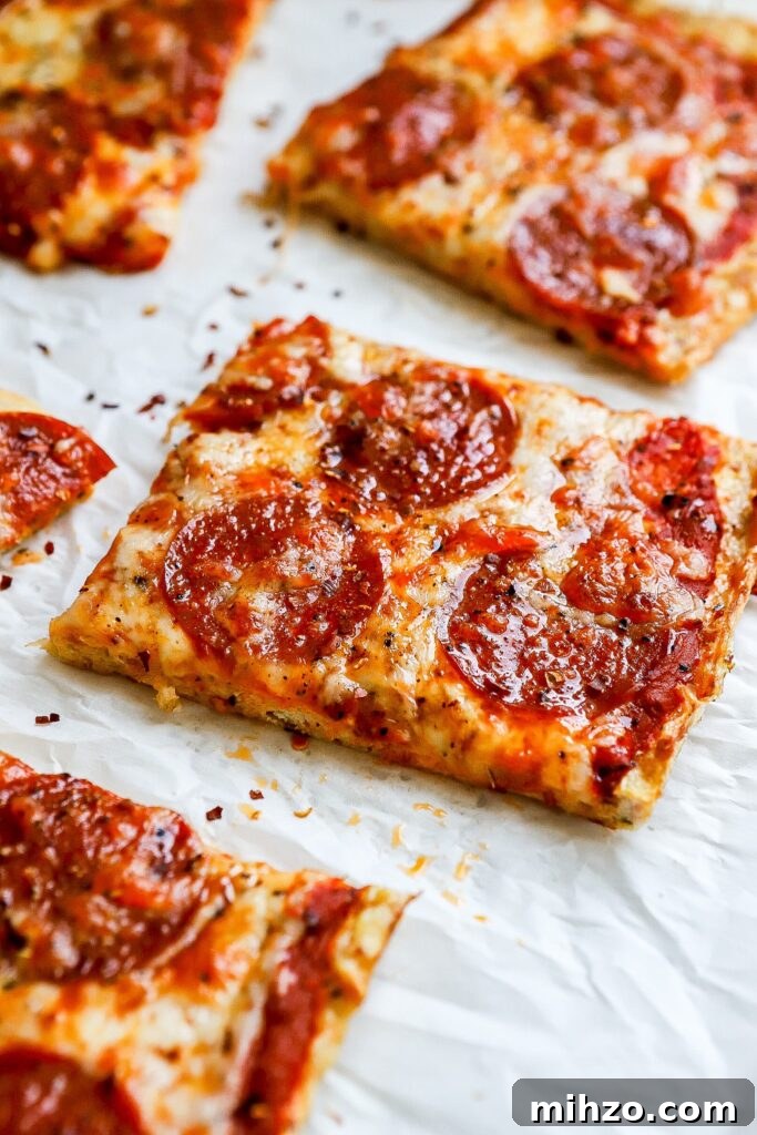 Side angle of chicken crust pizza with pepperoni on parchment paper