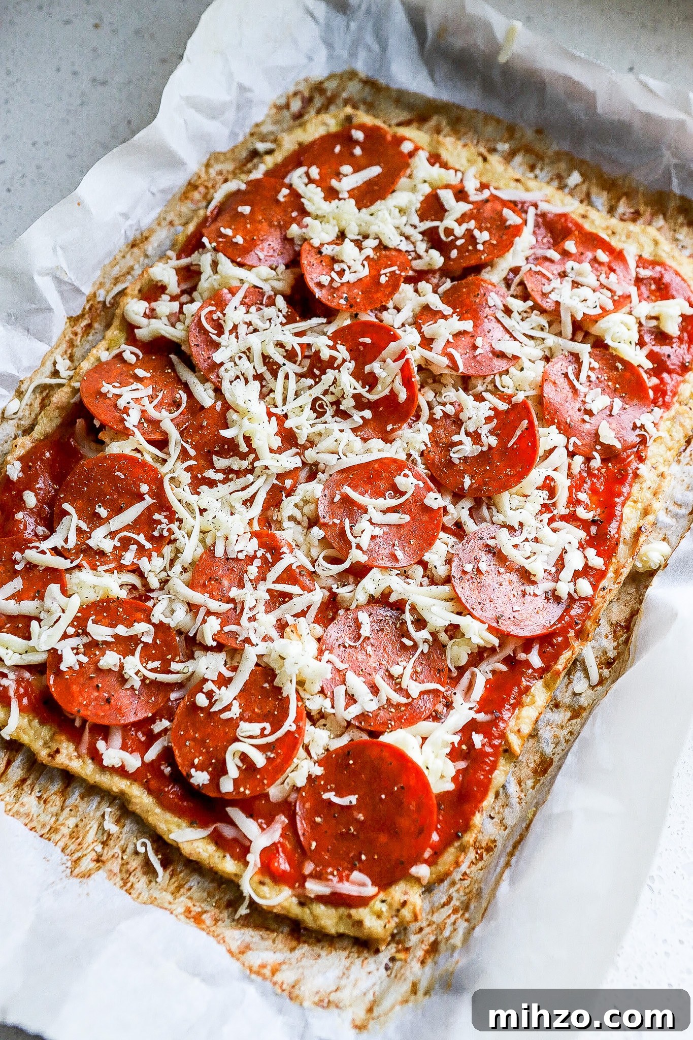 Side angle of pizza ready for the oven on a baking sheet.