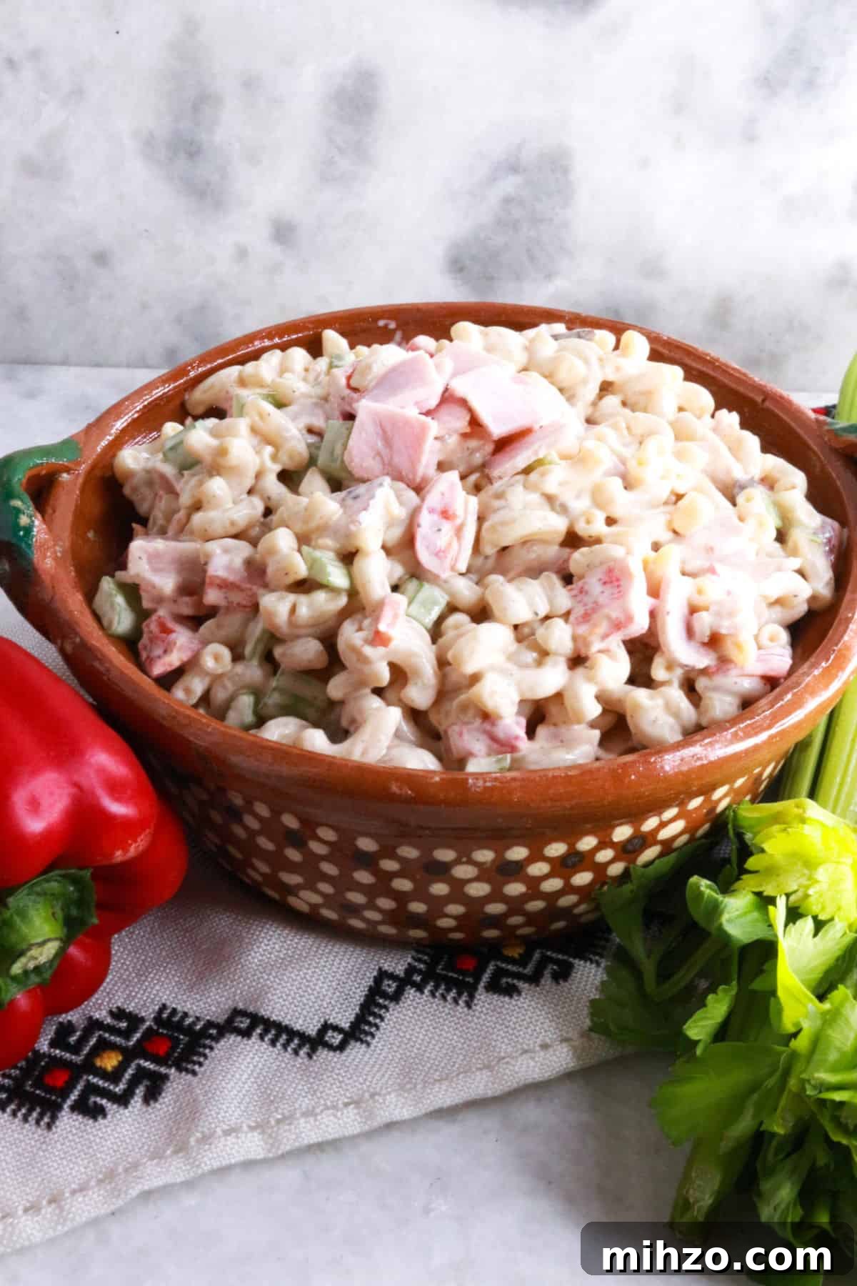 Mexican Macaroni Pasta Salad with Creamy Dressing 2 Ensalada de Coditos in a brown bowl with a red bell pepper and stalk of celery beside it.