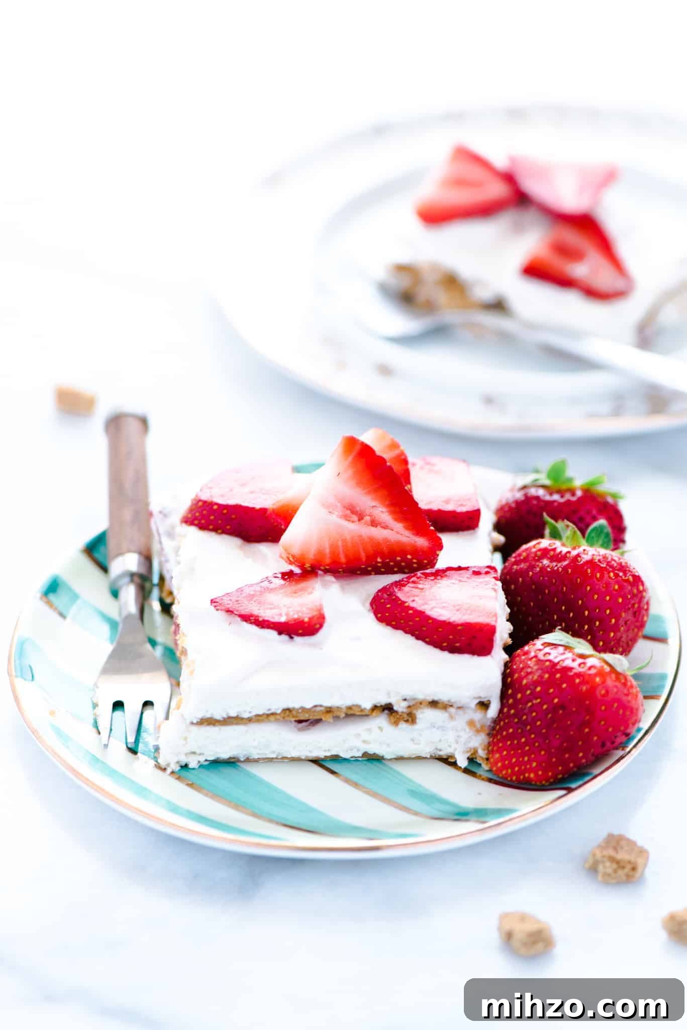 Gluten-Free Strawberry Icebox Cake Recipe for Summer Parties 2 A piece of Gluten Free Strawberry Icebox Cake on a green and white striped plate with a fork. Plate is garnished with whole strawberries.