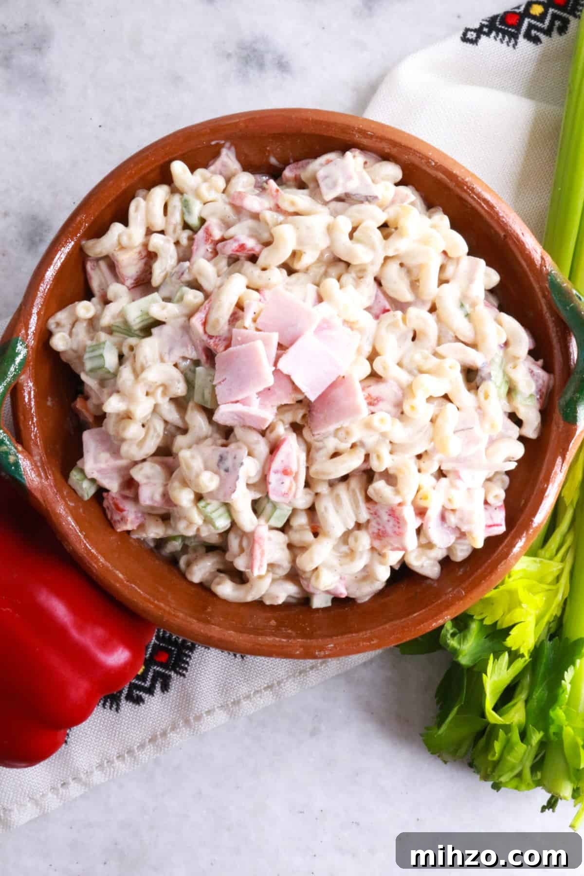 Mexican Macaroni Pasta Salad with Creamy Dressing 7 Ensalada de Coditos in a brown bowl with a red bell pepper and stalk of celery beside it.