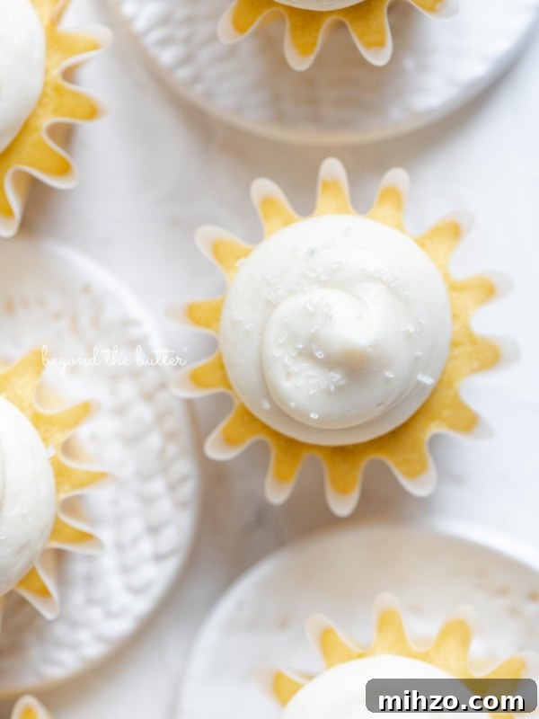 Single-Layer Funfetti Cake Recipe for Bright, Moist Celebration Cakes 14 Overhead image of vanilla cupcakes with vanilla buttercream frosting sprinkled with sparkling sugar grouped close together on white background and small ceramic plates.