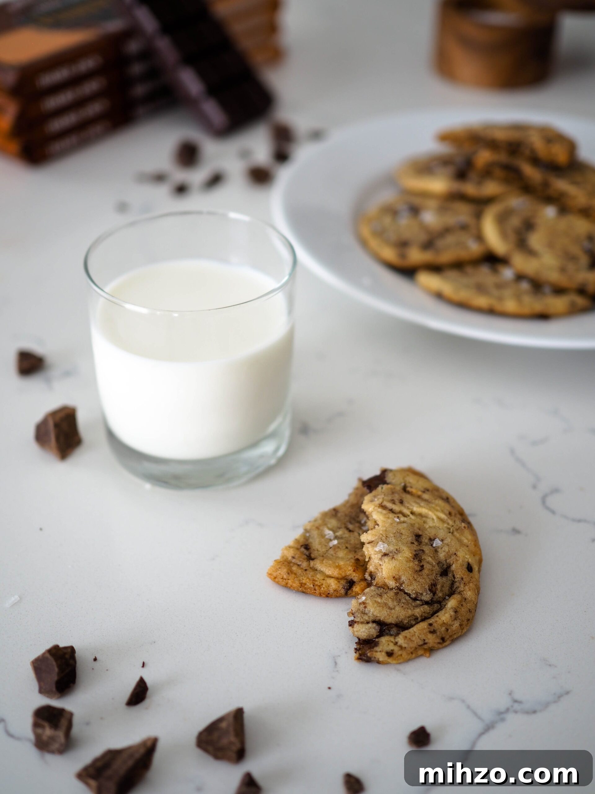 A glass of milk beside two halves of a chocolate chip cookie.