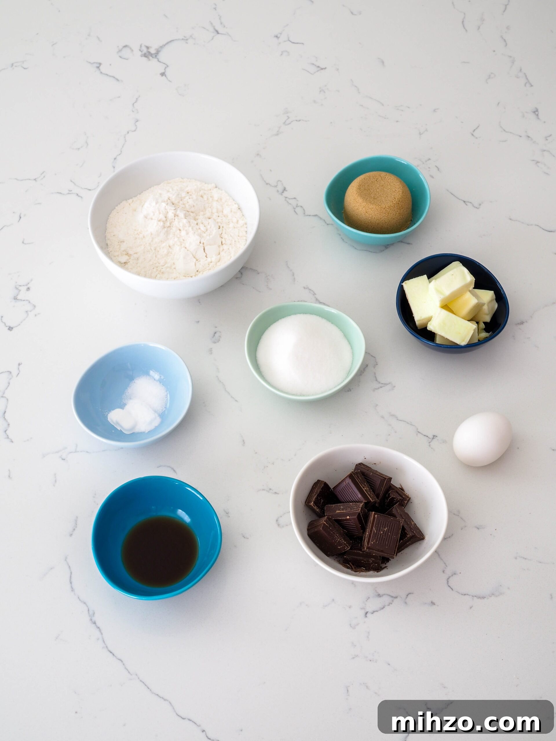 Flour, sugar, brown sugar, butter, an egg, chocolate chunks, vanilla extract, baking powder and soda, and salt on a counter.
