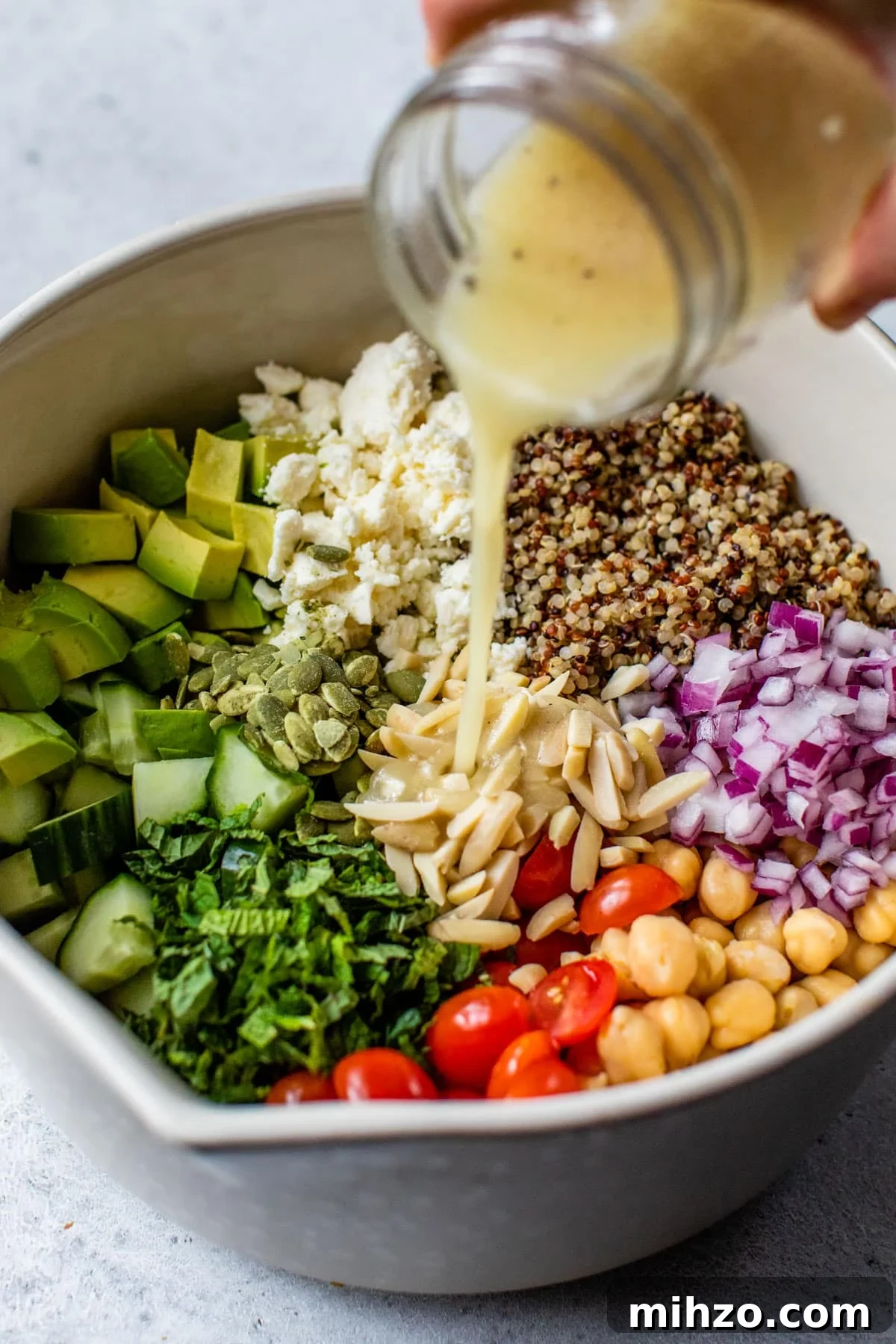 Zesty Lemon Quinoa Salad with Crispy Veggies and Herbs 4 bowl with quinoa, feta cheese, cucumber, and other vegetables inside and dressing being poured overtop