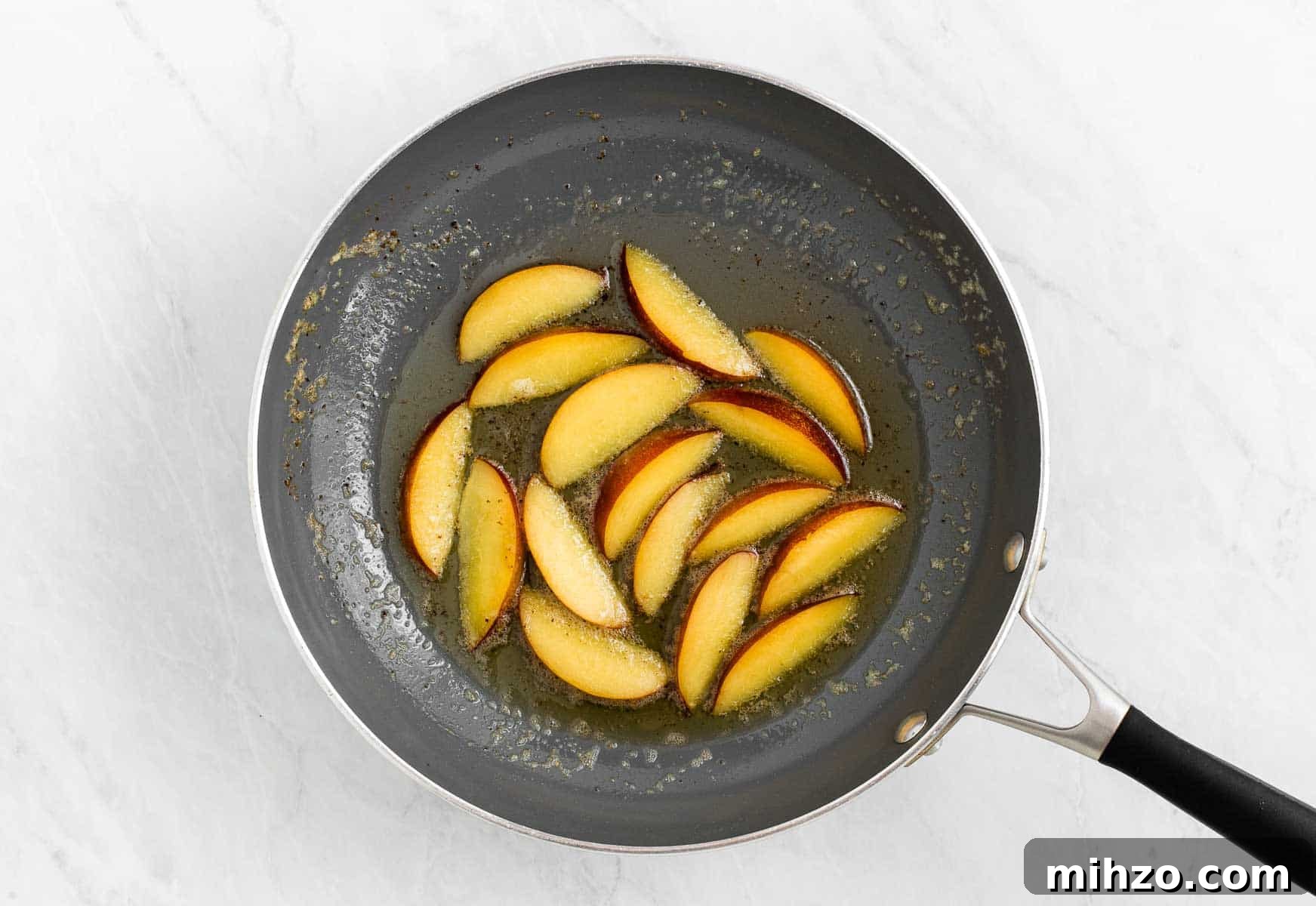 Nectarines sautéing in butter in a skillet.