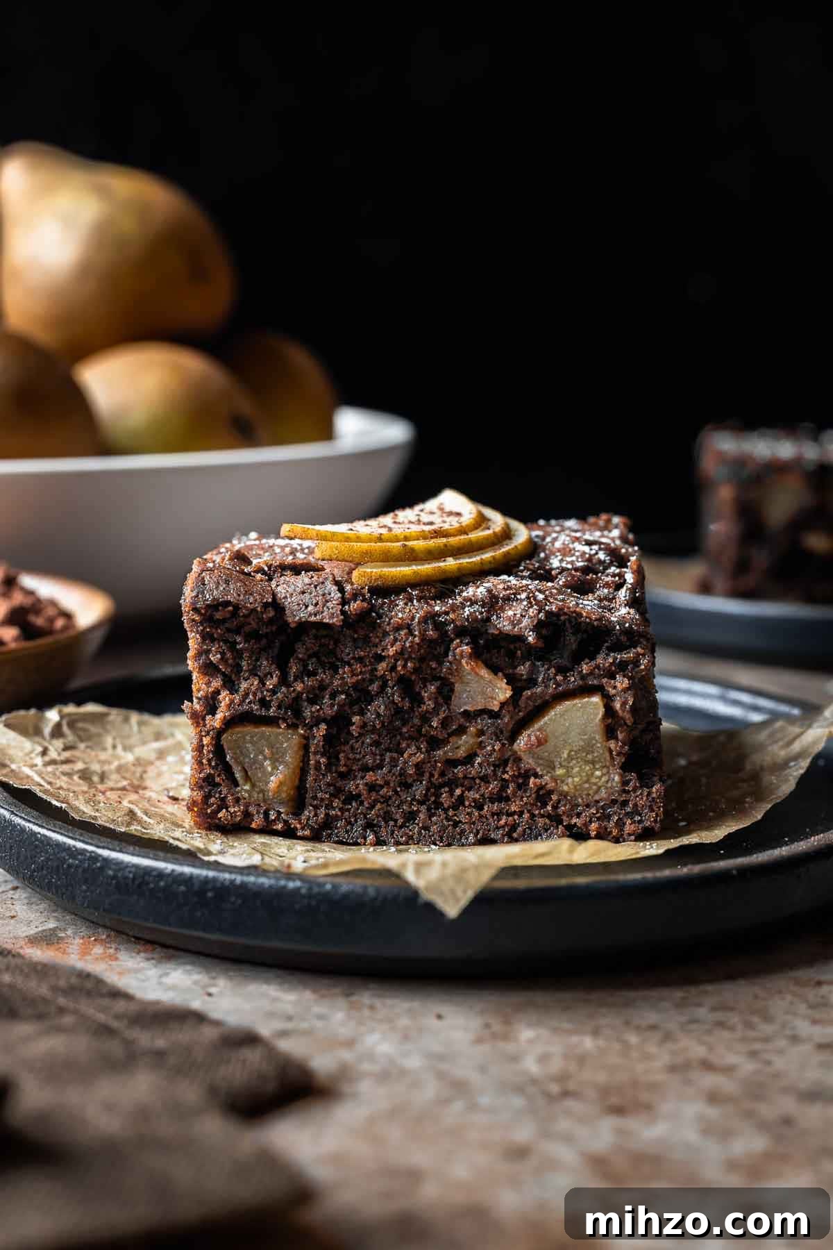 A square of chocolate pear cake from the side showing the crumb and fruit inside.
