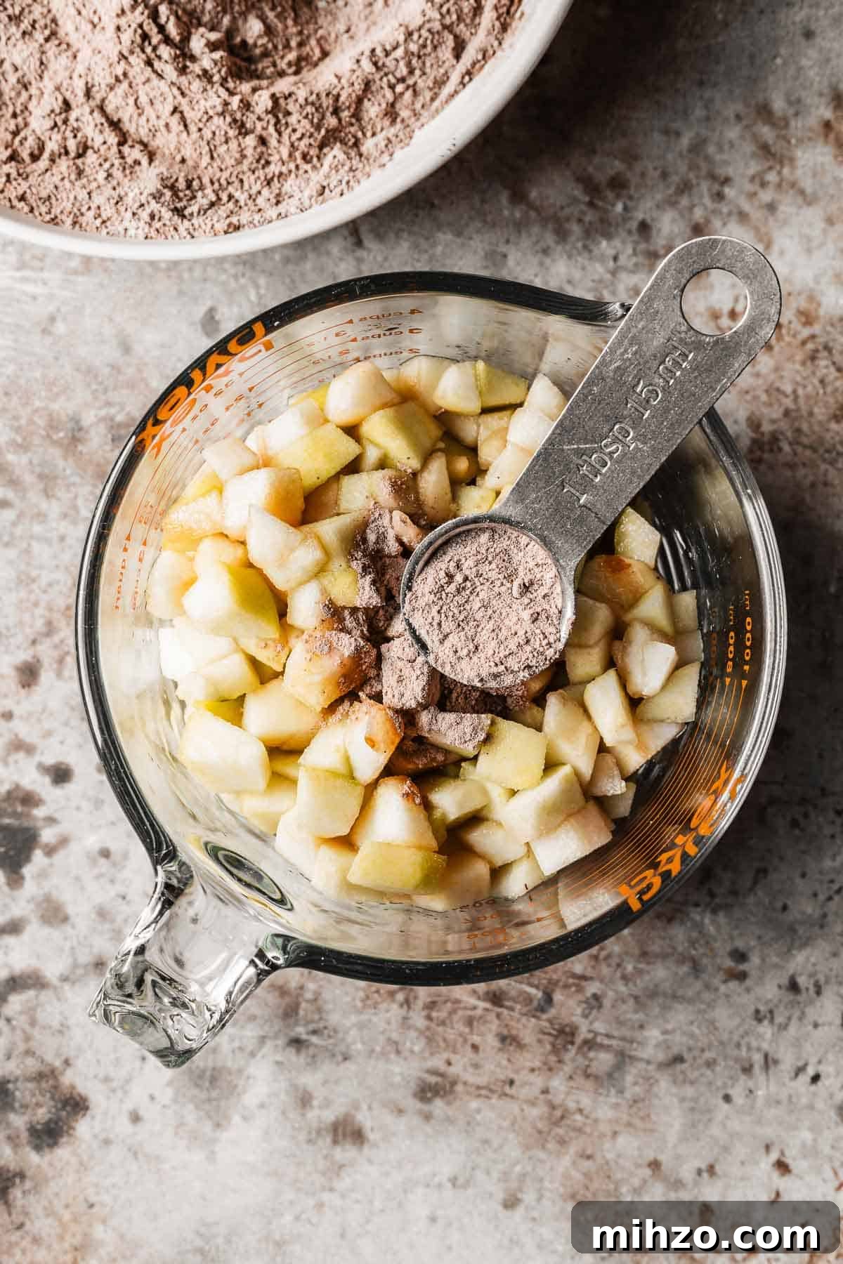 A glass measuring cup with diced pears and a tablespoon of flour mixture on top.