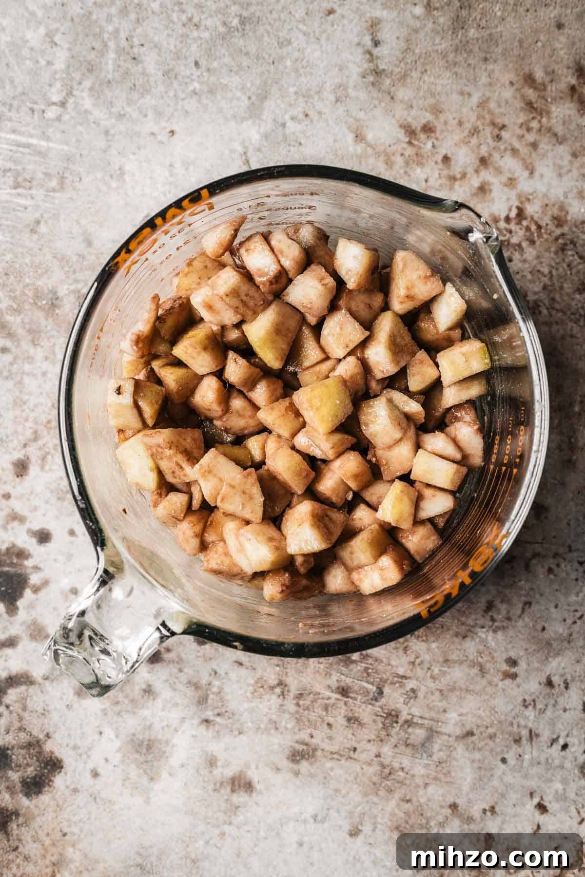 A glass measuring cup of diced pears coated in flour mixture.