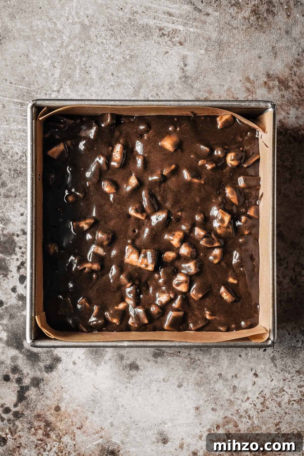 Chocolate pear cake batter in a parchment paper lined square pan.