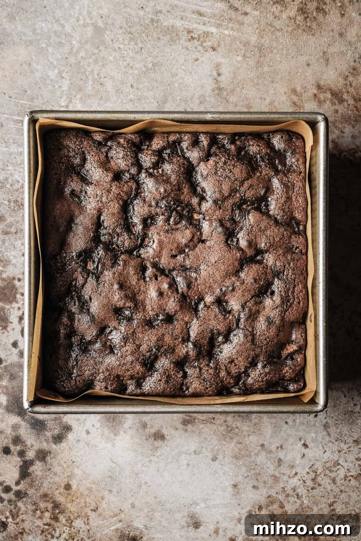 A baked chocolate pear cake in a square parchment lined metal pan.