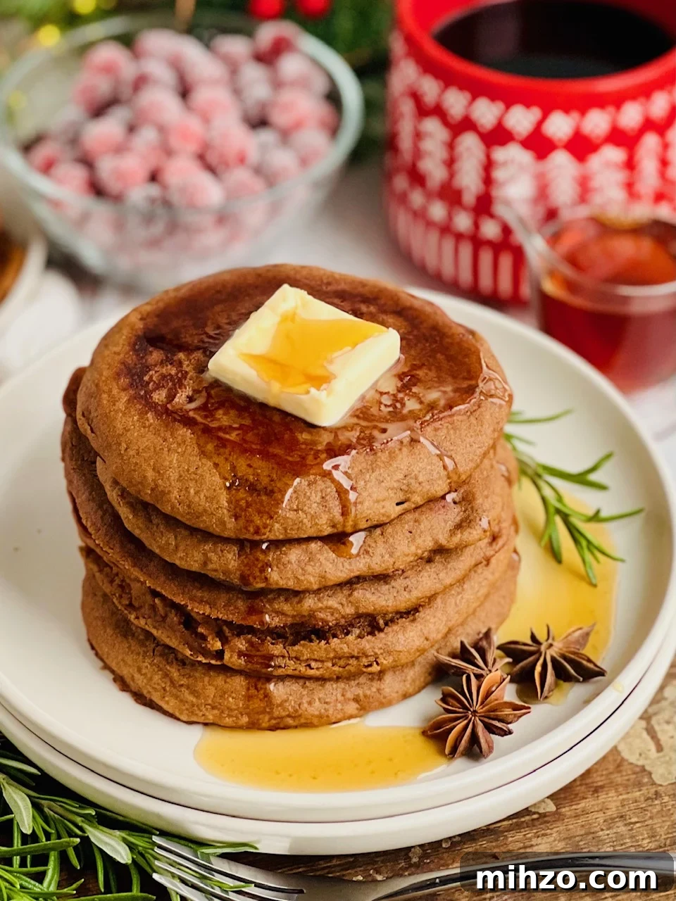Gingerbread Pancakes Recipe: Fluffy Spiced Holiday Pancakes 5 A white plate filled with dark brown colored round pancakes with a large square of melty butter and syrup running down the top.