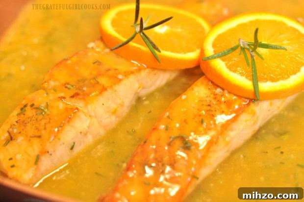 Two pieces of salmon with orange slices in skillet with sauce.