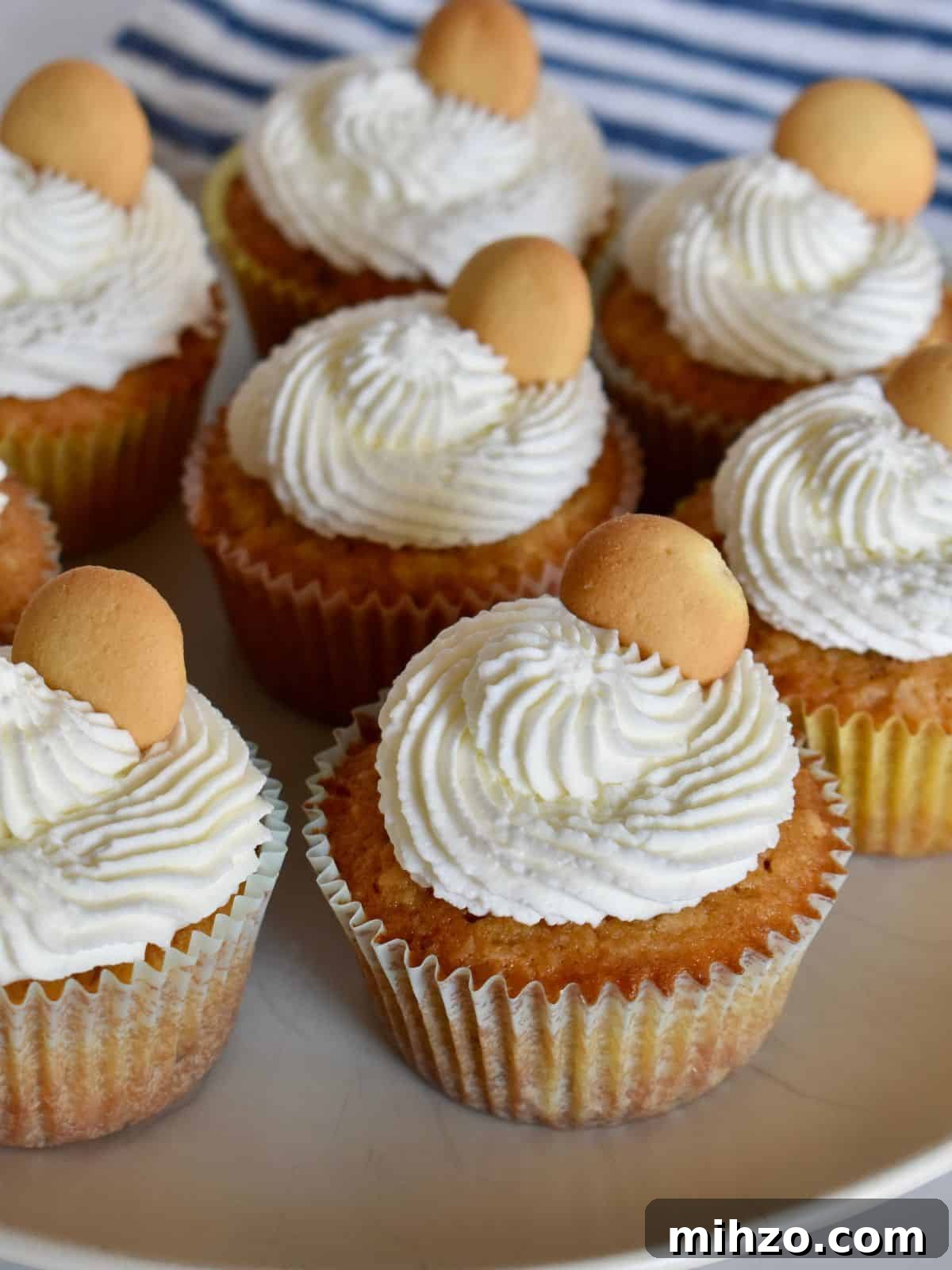 Classic Vanilla Wafer Cupcakes with Creamy Buttercream Frosting 2 Vanilla wafer cupcakes on a plate with a vanilla wafer on top and a striped cloth in the background.
