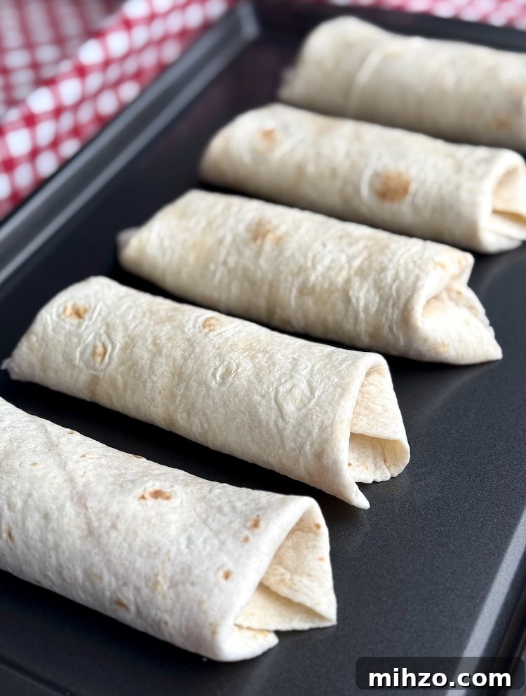 How to Make Pizza Burritos at Home — Fusion Recipe and Tips 6 Pizza burritos rolled and stuffed in flour tortillas on baking pan.