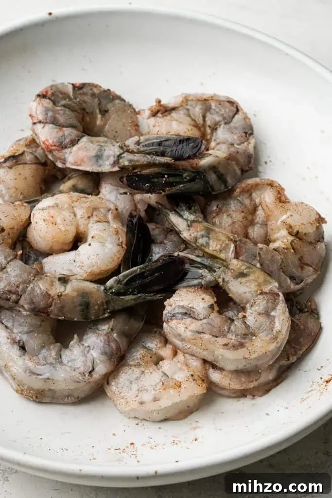 coconut shrimp recipe uncooked shrimp in a shallow bowl seasoned with five spice, garlic, and salt