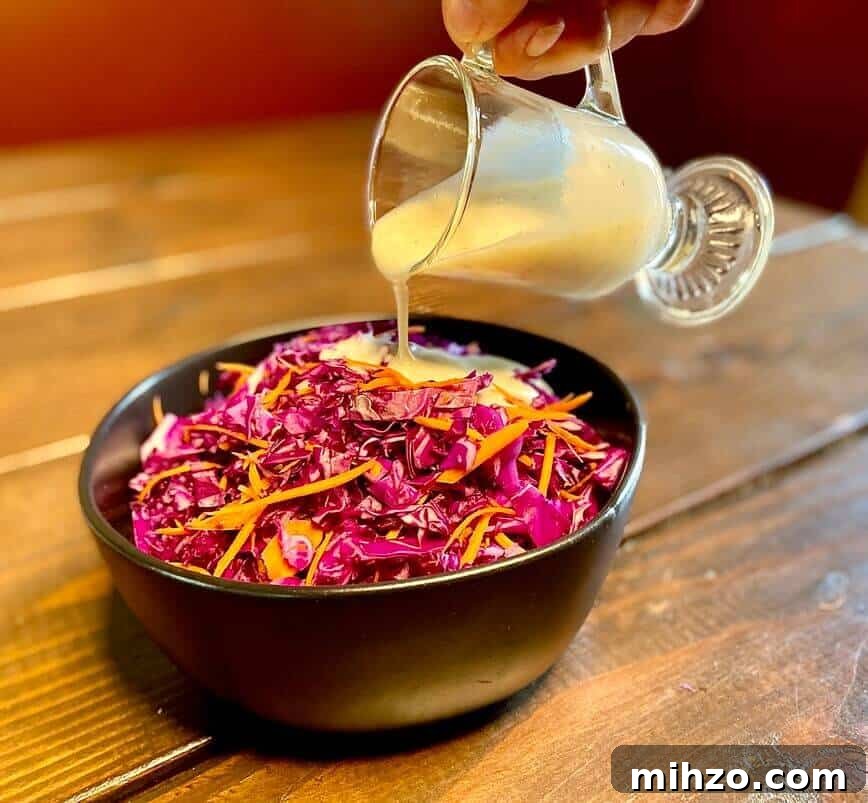 Classic Creamy Homemade Coleslaw Recipe You’ll Love 7 Pouring dressing over cabbages and carrots.