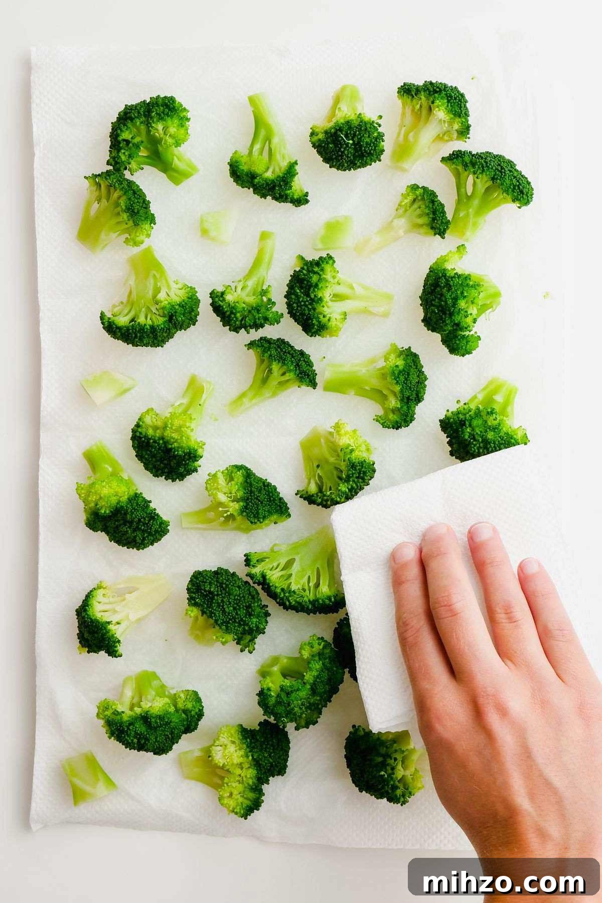 Blanch Broccoli Quickly: Perfectly Crisp, Bright Green Every Time 9 image of a hand patting dry scattered broccoli florets on white parchment paper