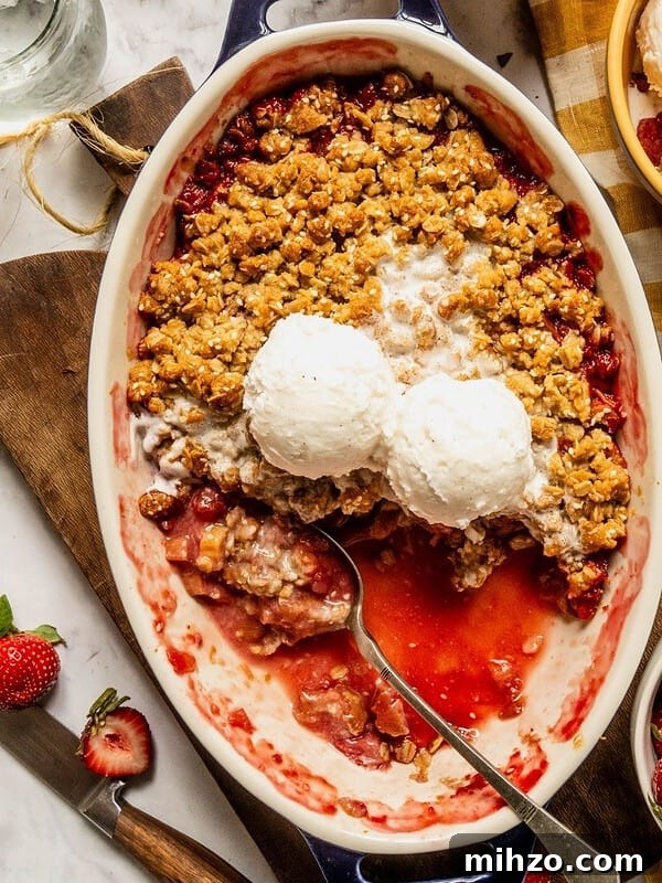 Strawberry rhubarb crisp with a tahini sesame topping in an oval dish with 2 scoops of ice cream.
