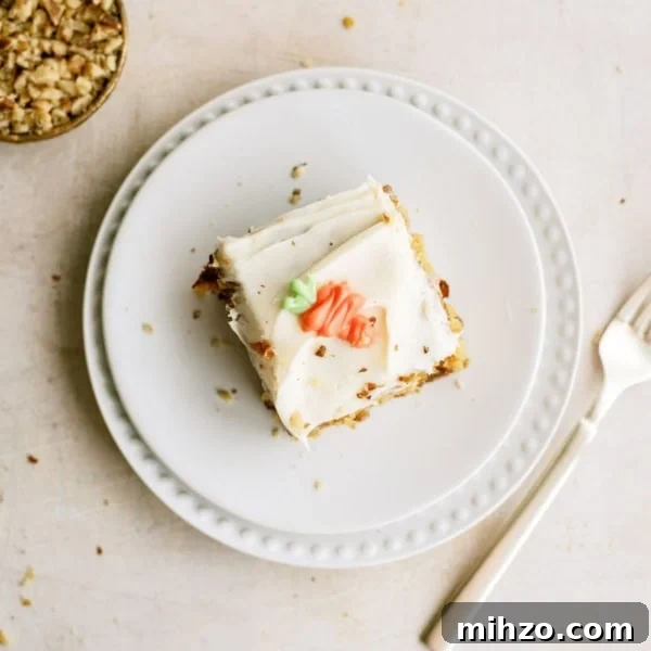 A slice of frosted cake with decorative icing sits on a white plate next to a fork; a small bowl of chopped nuts is nearby.