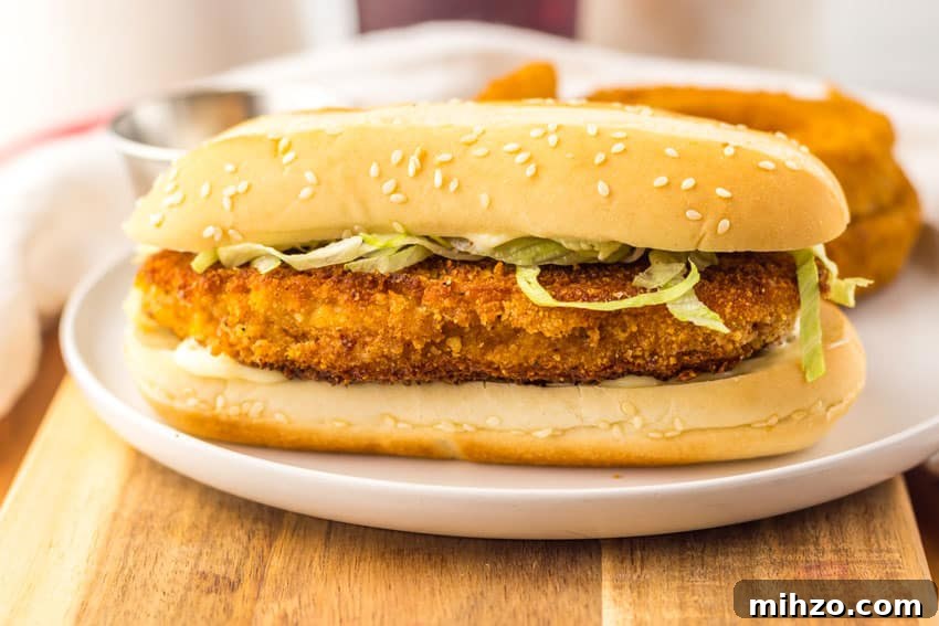 copycat burger king original chicken sandwich on a white plate with fried onion rings in the background