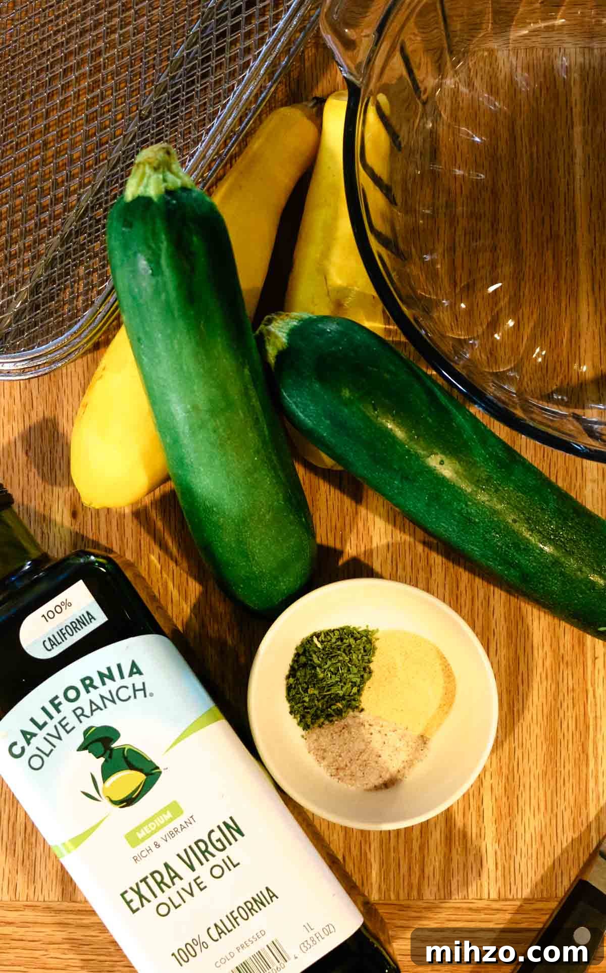olive oil, zucchini, and yellow squash with seasonings on a cutting board.