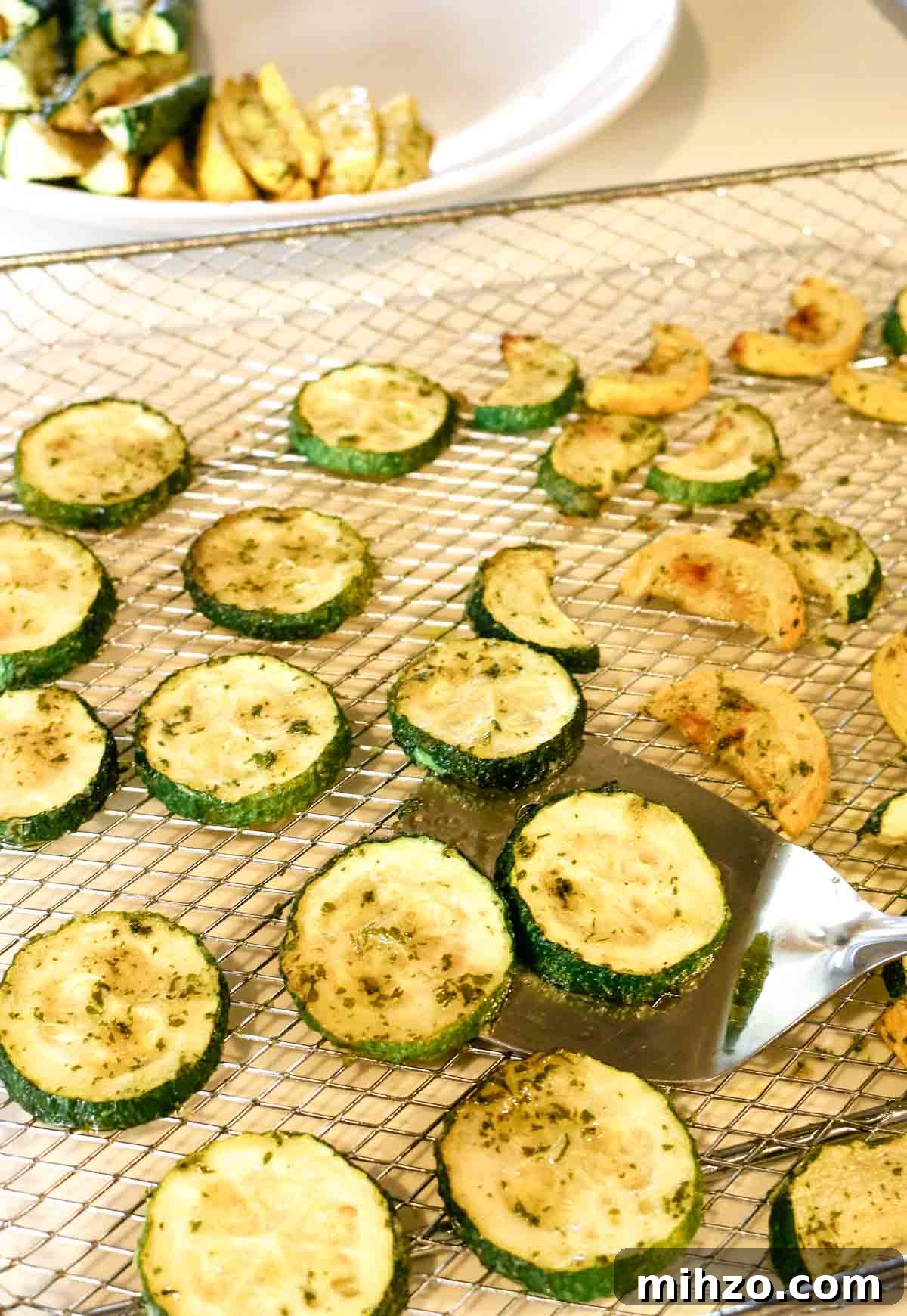 roasted zucchini on air fryer trays with spatula.