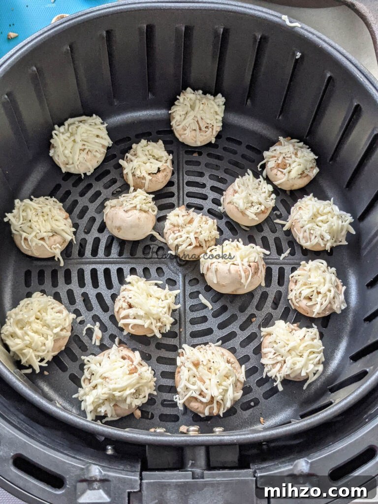Mushroom caps stuffed and garnished with grated cheese ready for air frying in air fryer basket.