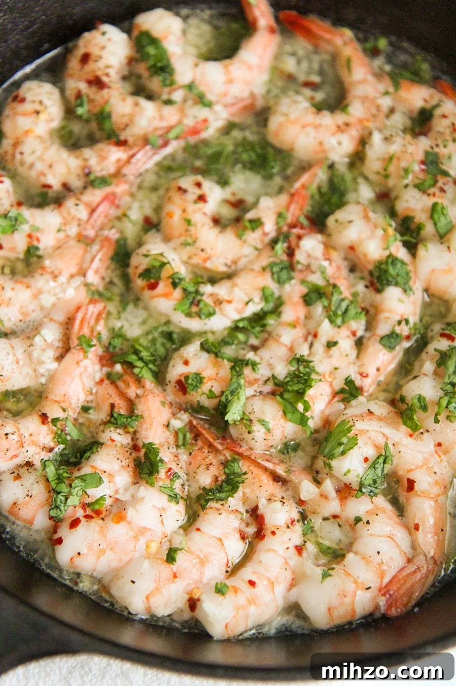Garlic Butter Baked Shrimp Scampi Recipe for Dinner 2 baked shrimp with parsley in a cast iron skillet up close.