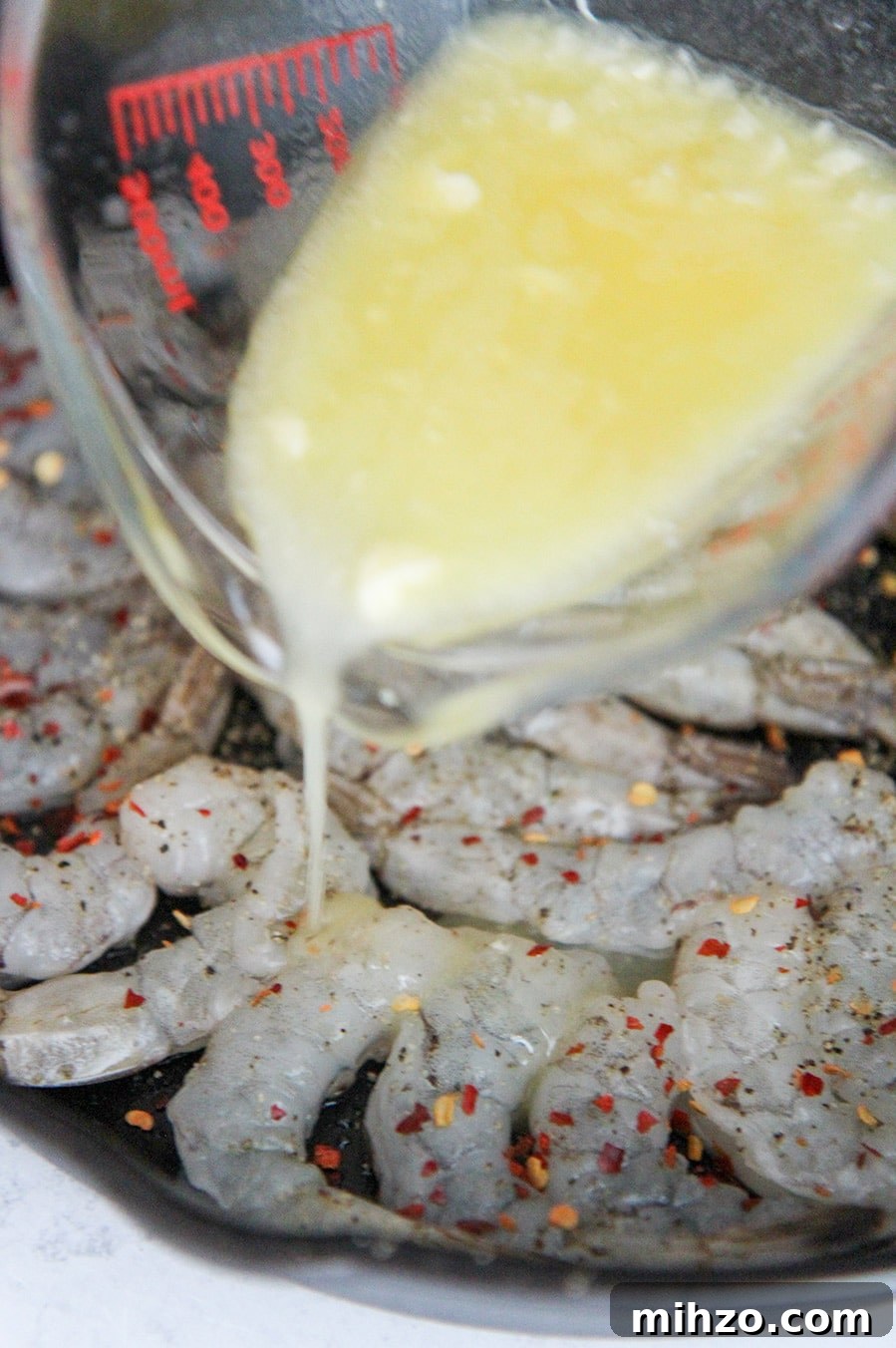 Garlic Butter Baked Shrimp Scampi Recipe for Dinner 3 a measuring cup pouring melted butter over raw shrimp.
