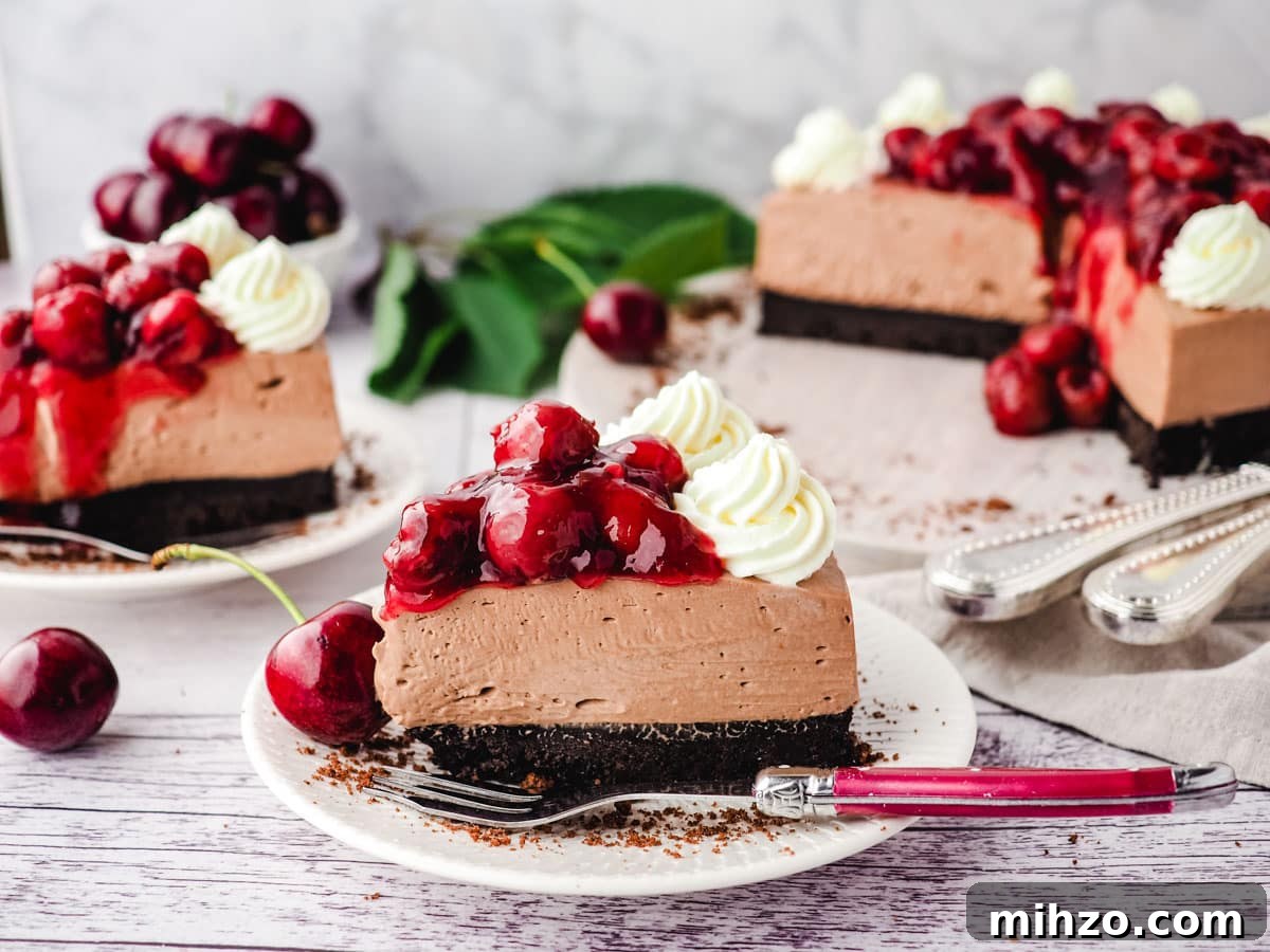 Slice of chocolate cherry cheesecake with a fork and rest of cake in the background.