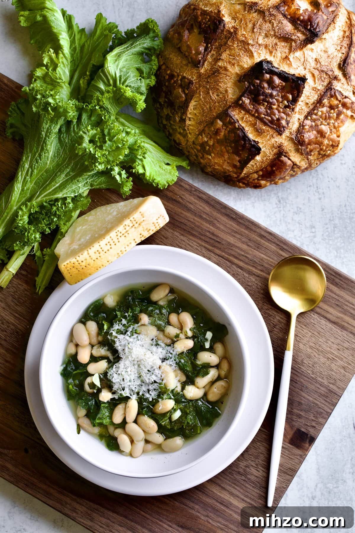Italian beans and greens soup in a bowl on a wooden board with crusty bread .