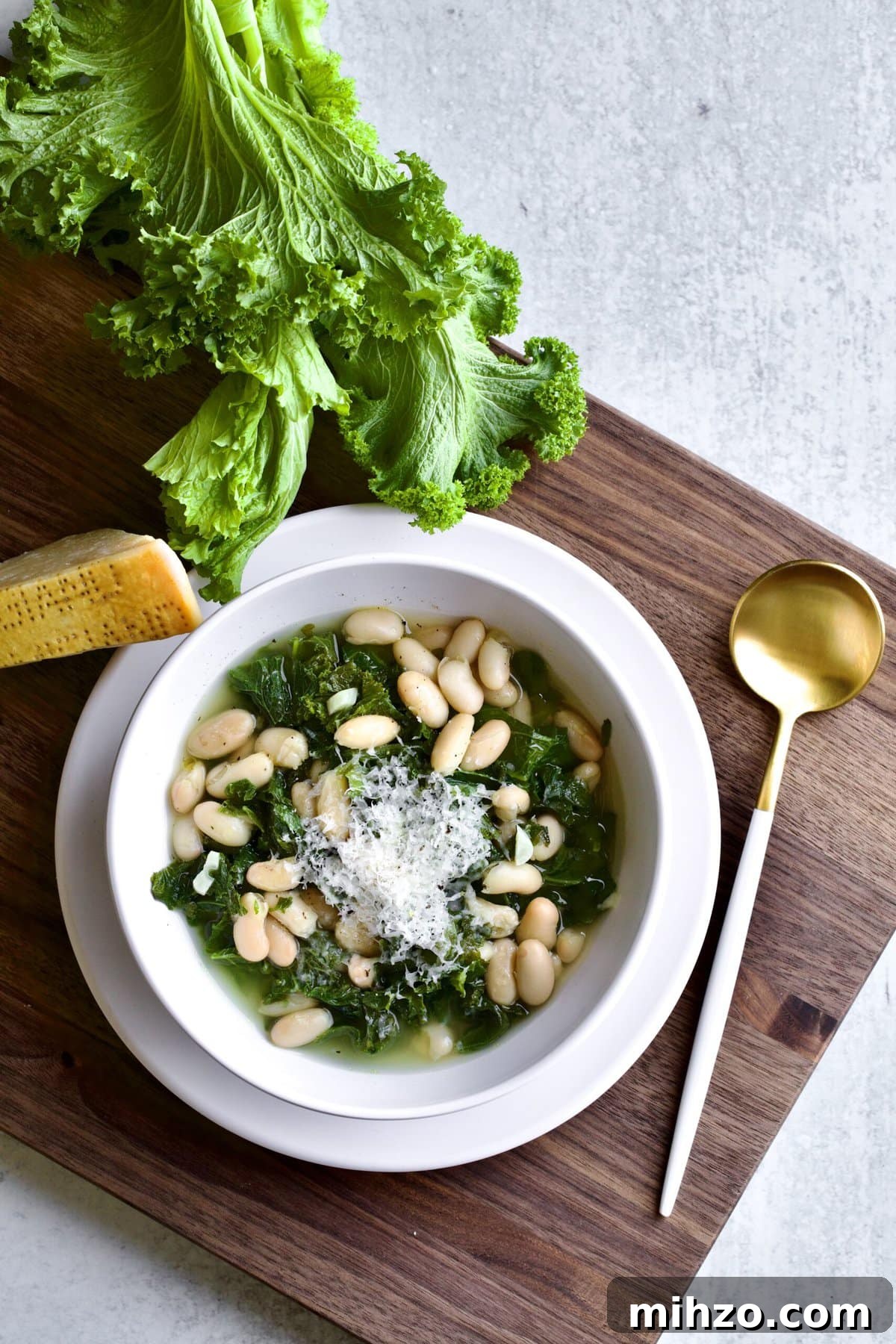 A bowl of beans and greens with a spoon to the side and some escarole in the corner. 
