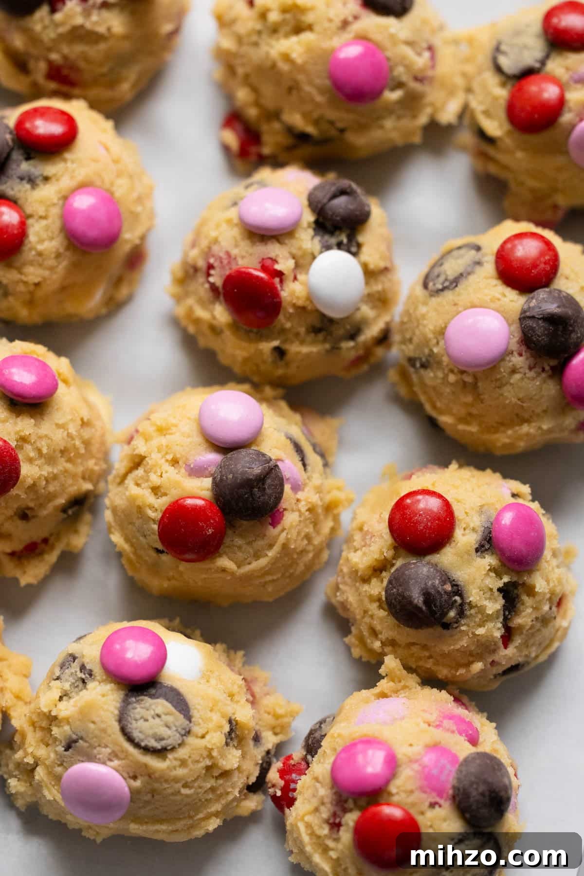 Valentine’s Day M&M Cookie Recipe: Festive Chocolate Cookies 6 cookie dough on parchment paper garnished with m&ms and chocolate chips on top.