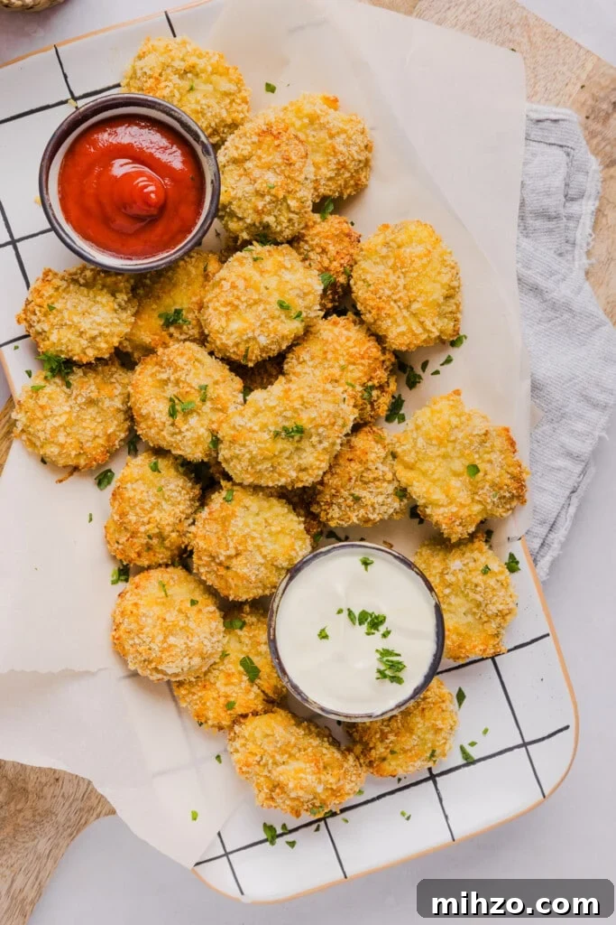 Cauliflower chicken nuggets on a countertop with parchment paper and two dips.