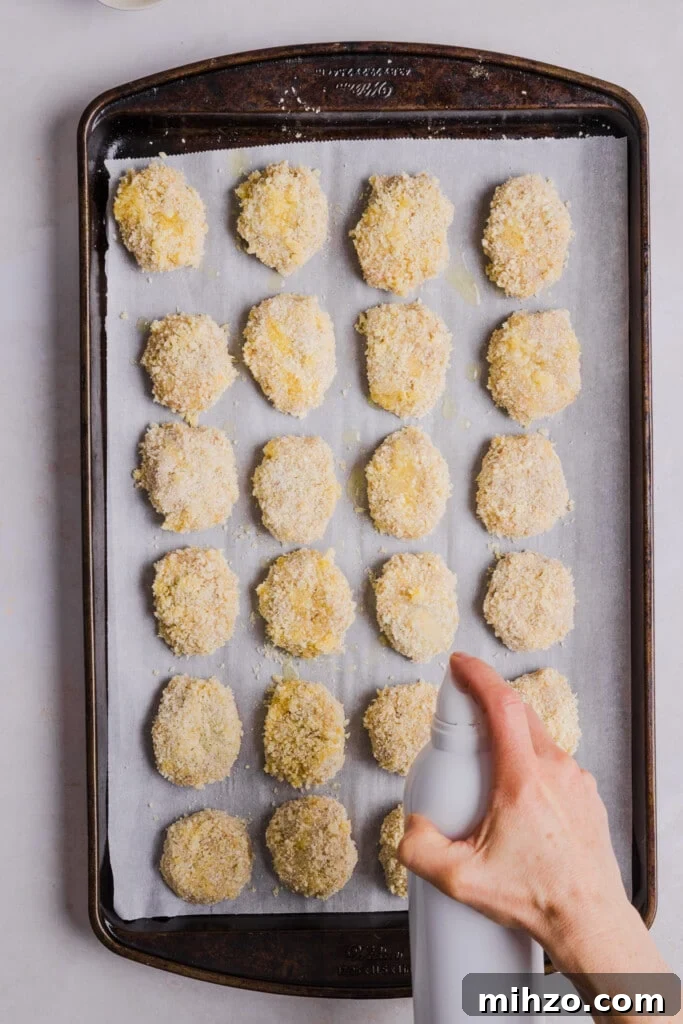 Cauliflower chicken nuggets being sprayed with cooking spray.