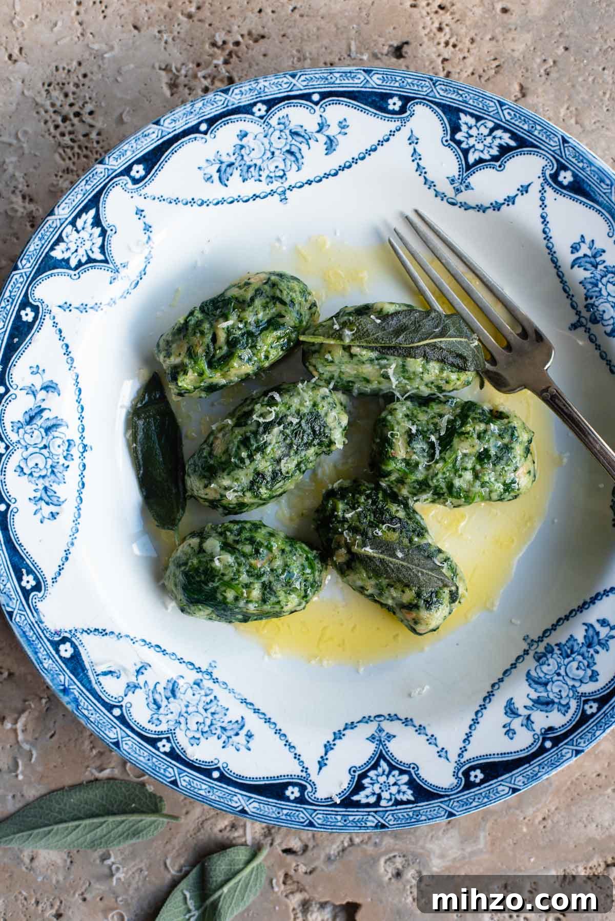 An overhead shot of Strangolapreti (Italian bread dumplings) on a blue and white plate sitting on a stone work surface.