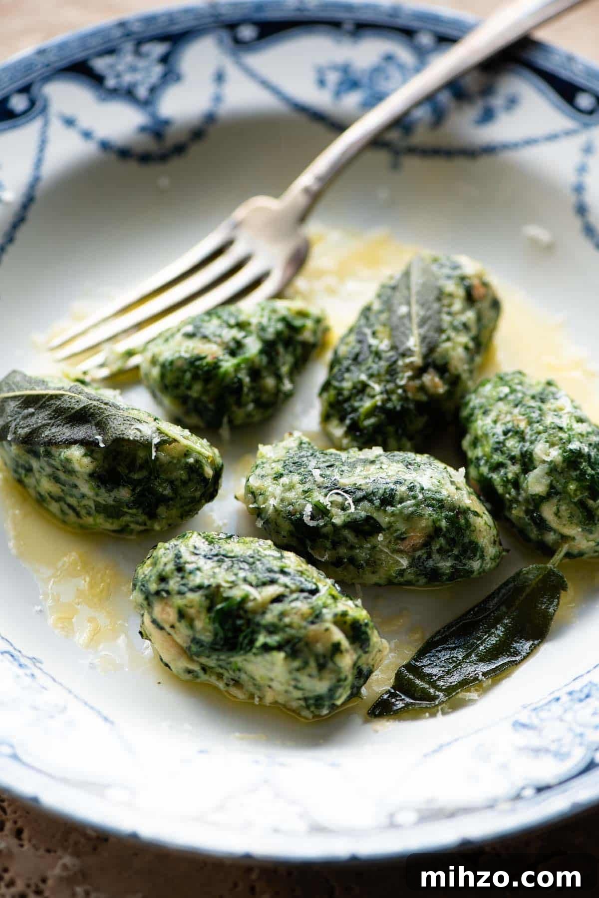 A side shot of Strangolapreti (italian bread dumplings) on a plate with butter and sage.