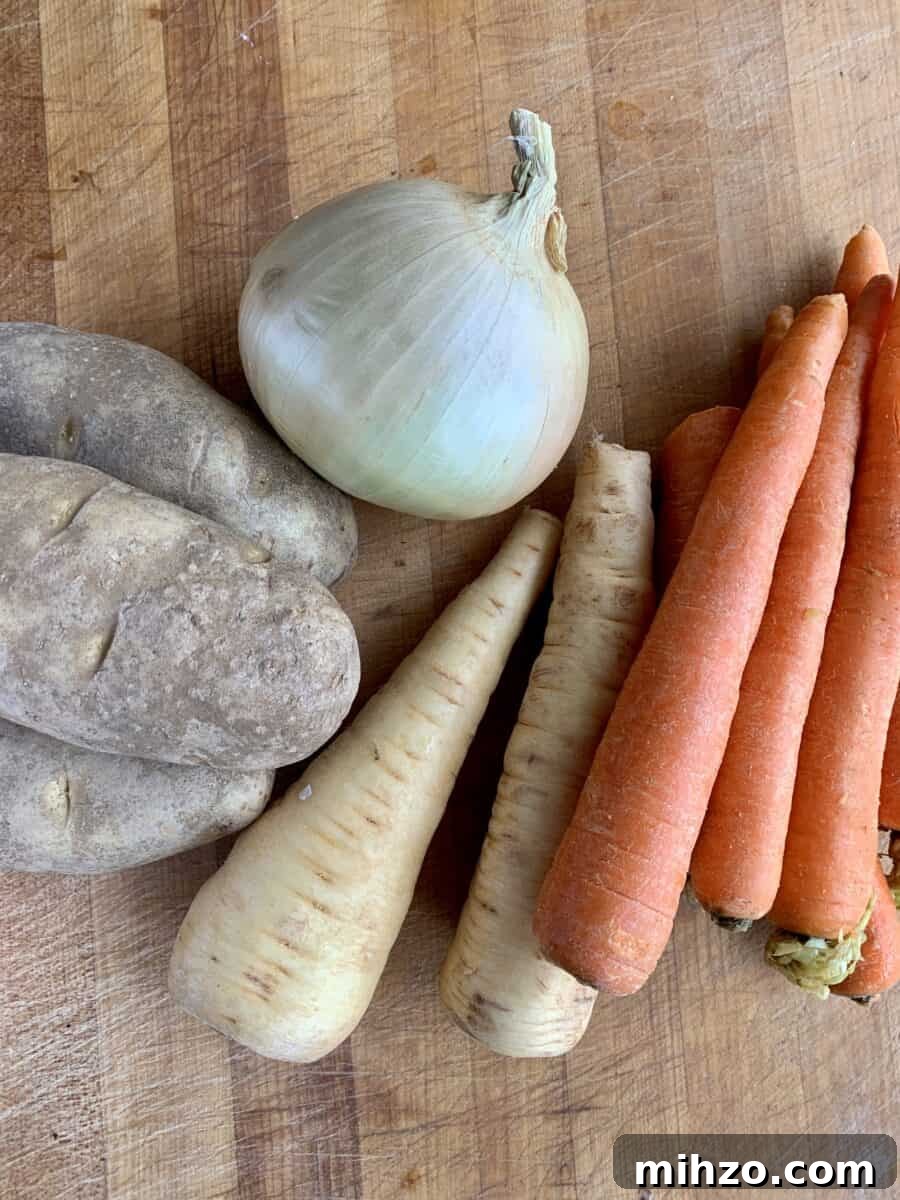 Classic Irish Beef Stew Recipe for Tender, Rich Flavor 3 Potatoes, onion, parsnips and carrots on a cutting board.