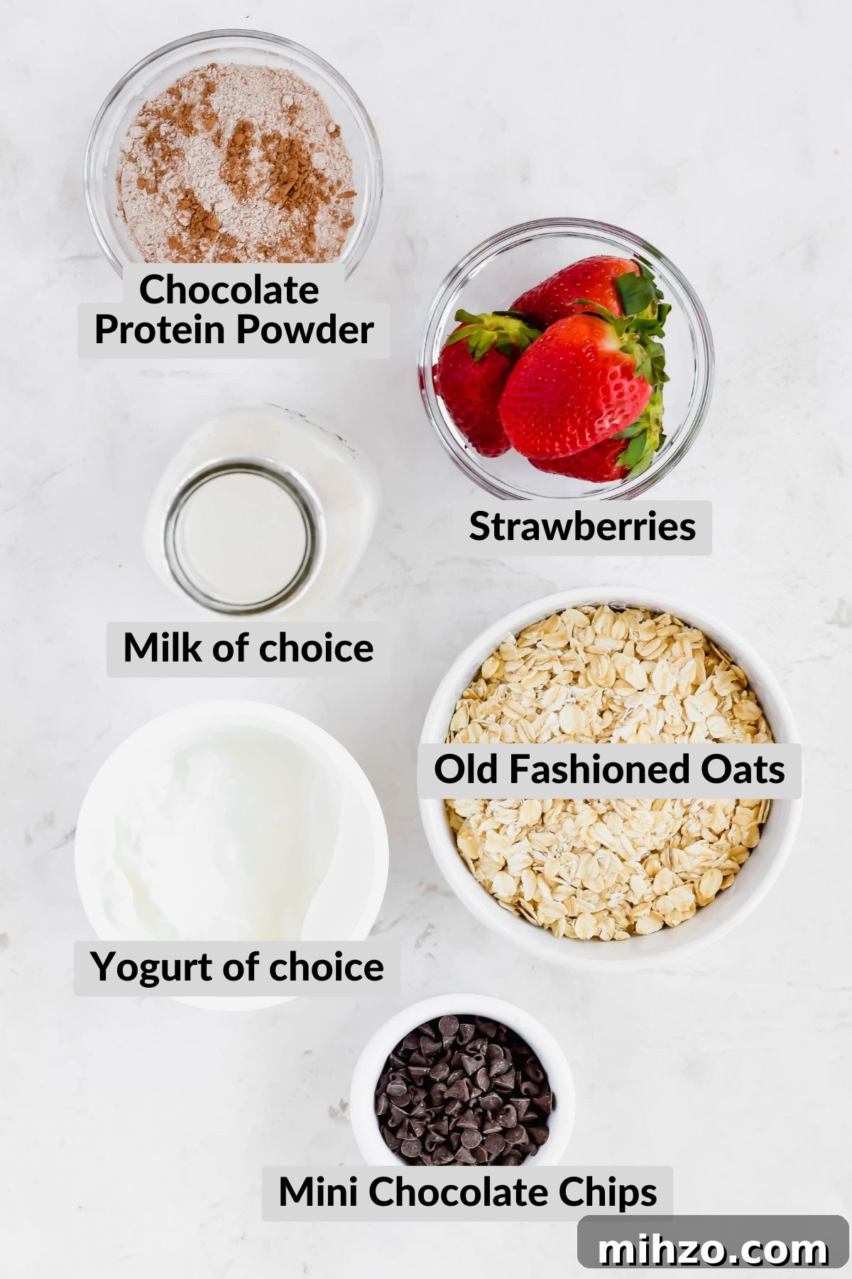 Chocolate-Strawberry Overnight Oats Recipe for Creamy Mornings 3 Bowls of chocolate protein powder, fresh strawberries, rolled oats, mini chocolate chips, yogurt, and a tall jug of milk.