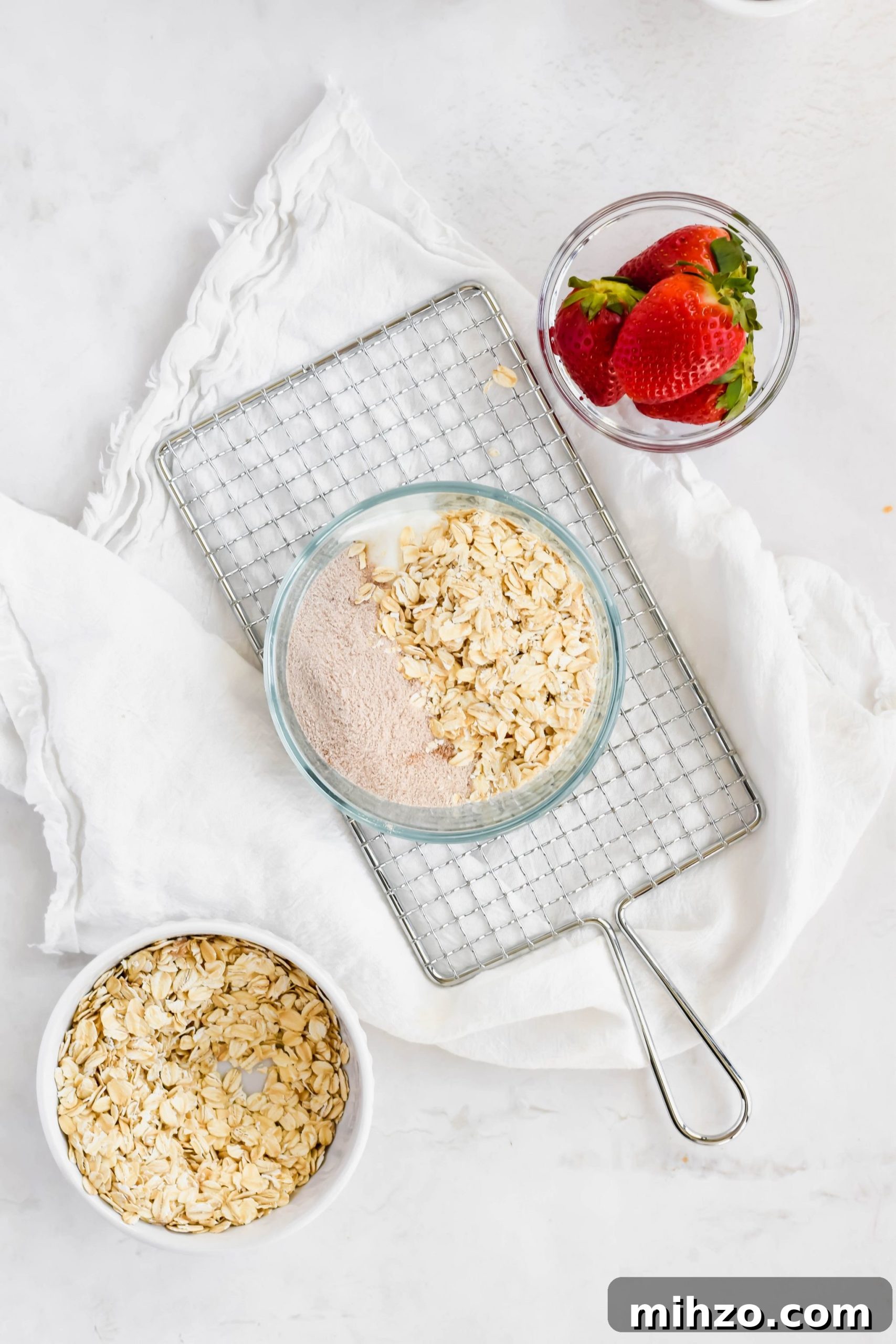 Chocolate-Strawberry Overnight Oats Recipe for Creamy Mornings 5 Strawberry Chocolate Overnight Oats ingredients in a small glass bowl next to a bowl of rolled oats and a bowl of fresh strawberries.