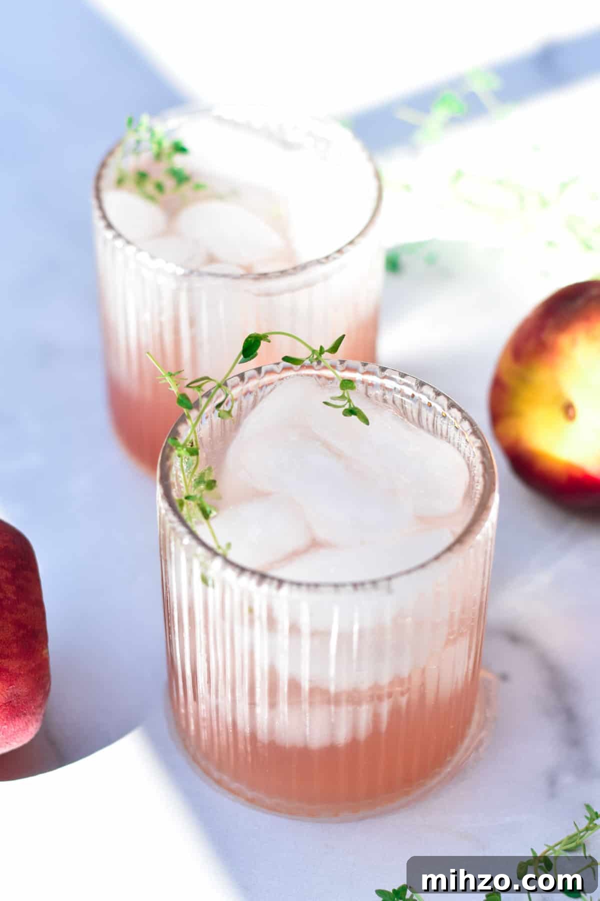 Refreshing Peach Mocktail Recipe for Summer Parties 6 Two peach mocktails next to fresh peaches and fresh thyme.