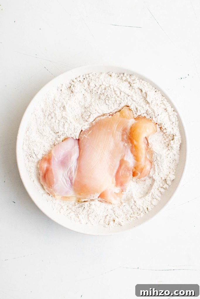 Chicken thigh in a dish of seasoned flour.