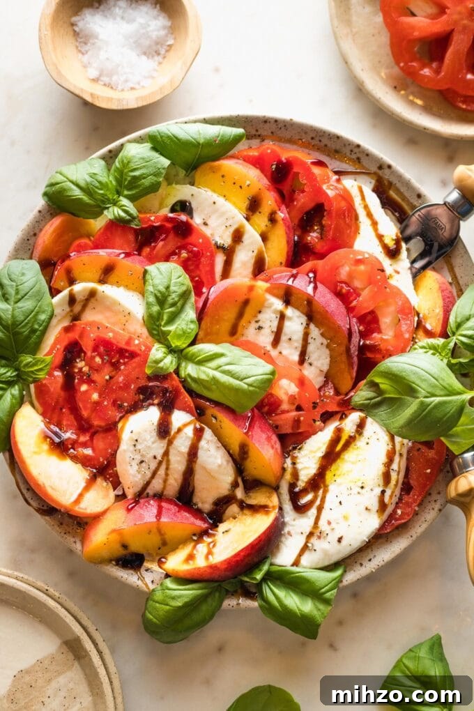 Earth-toned plate filled with a peach Caprese salad drizzled with balsamic glaze and fresh basil leaves.