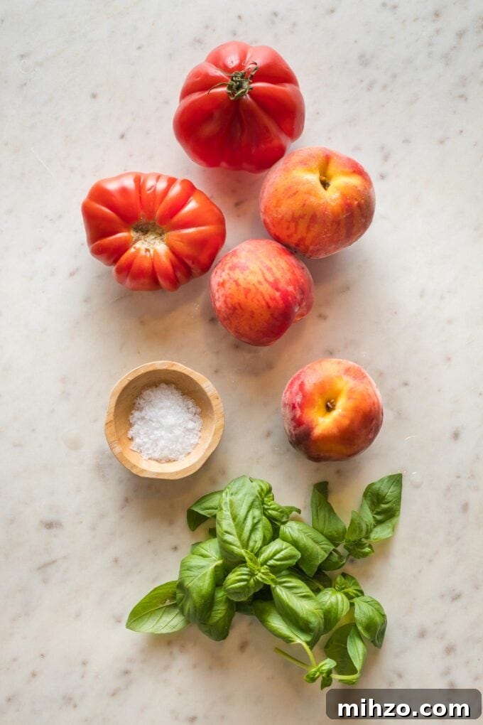 Heirloom tomatoes, peaches, sea salt, and fresh basil leaves scattered on a white countertop.