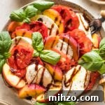 Earth-toned plate filled with a peach Caprese salad drizzled with balsamic glaze and fresh basil leaves.