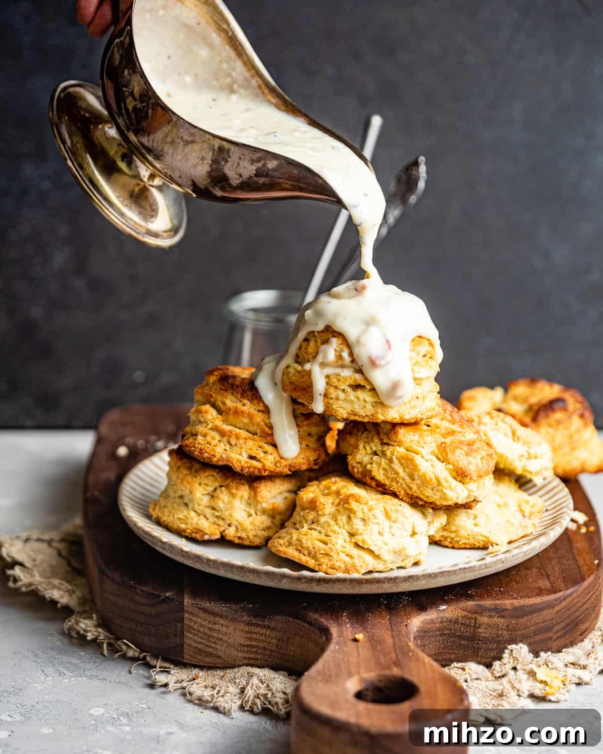 Creamy White Pepper Gravy Recipe for Biscuits and Roast 2 White gravy in a gravy boat being poured on top of a plate of of biscuits.