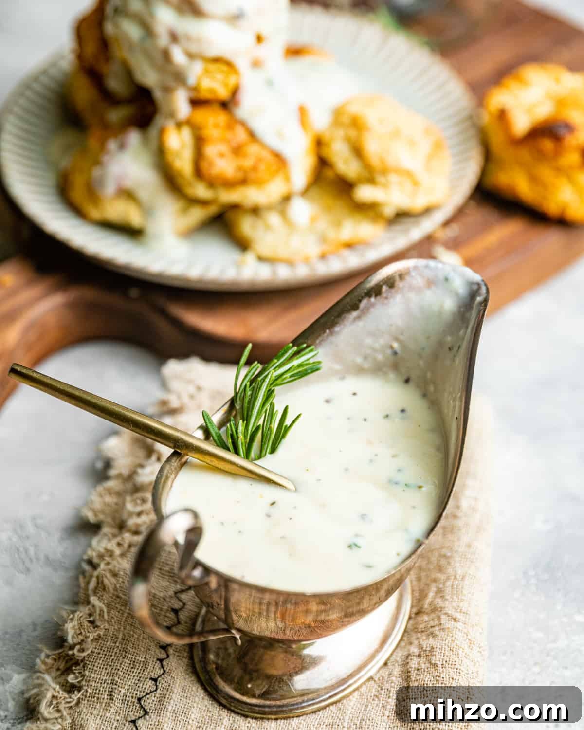 Creamy White Pepper Gravy Recipe for Biscuits and Roast 3 up close photo of white gravy in a gravy boat garnished with rosemary.
